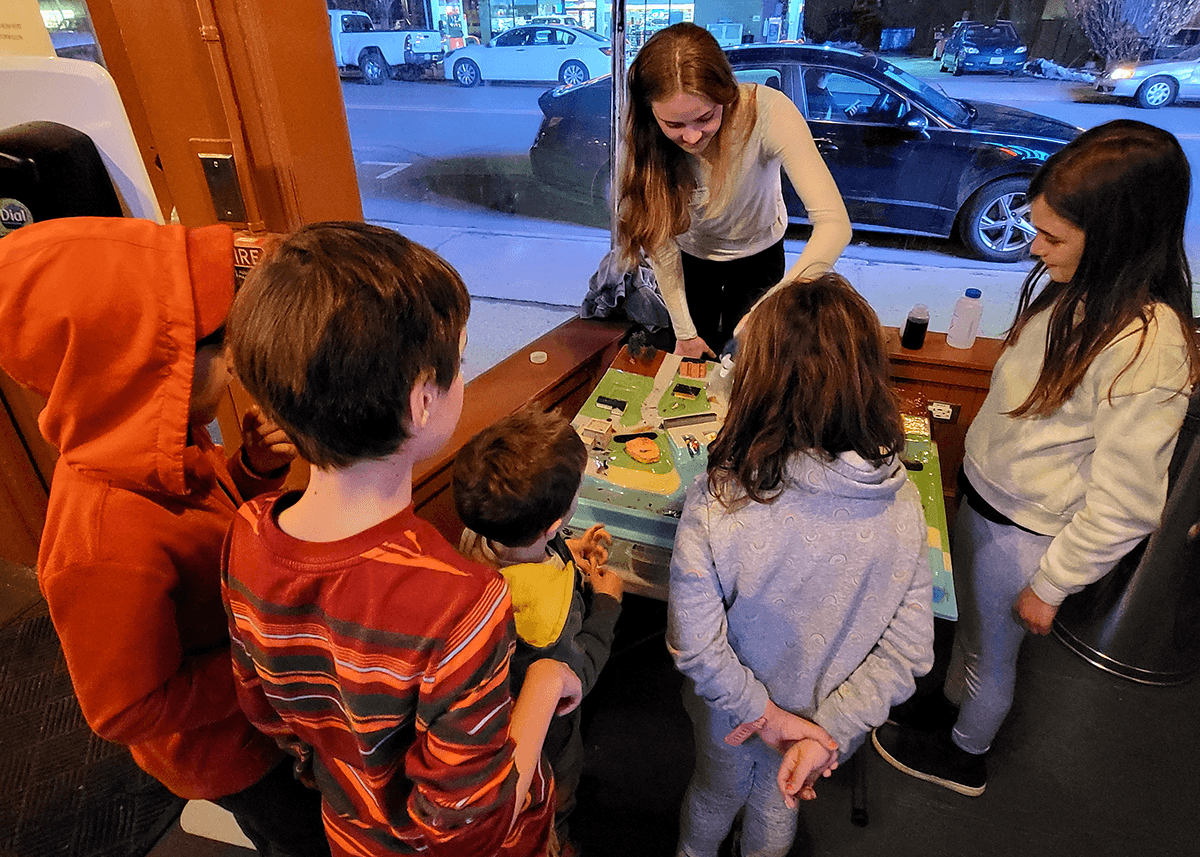 Kids and a volunteer gather around a table at the Cabot Theatre in Beverly, Massachusetts