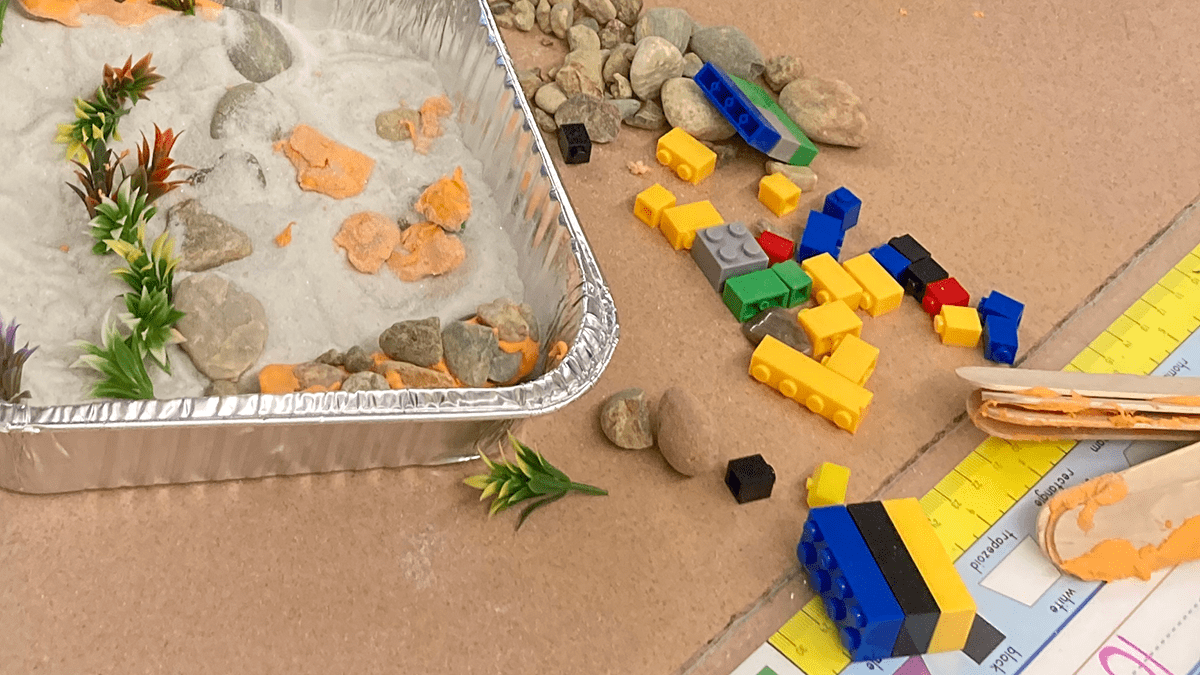 Erosion activity on top of a table with board game pieces surrounding an aluminum basin.