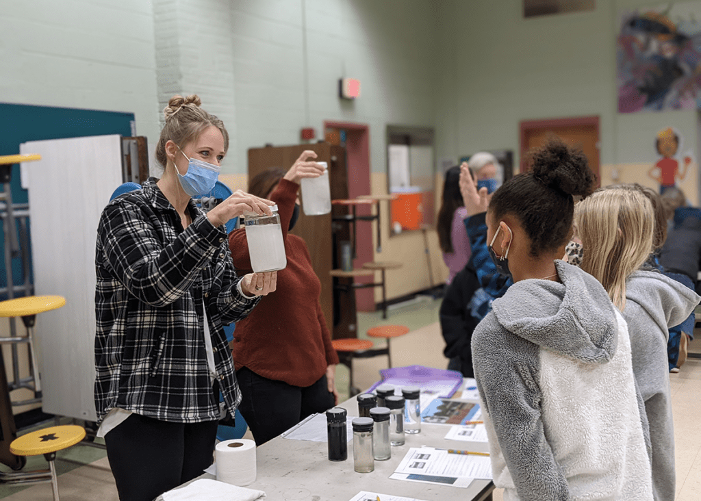 A volunteer teaches kids about healthy waterways in a school gymnasium.