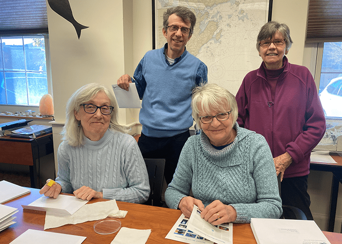 A group of four volunteers help stuff envelopes for year end mailers.