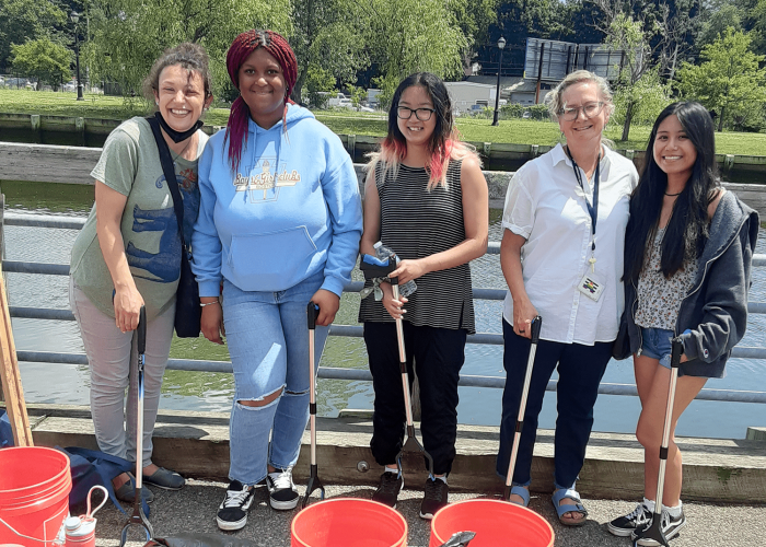 Salem Prep students and teacher standing in front of North River on commercial street, after a cleanup. Buckets in the foreground and everyone is holding a grabber.